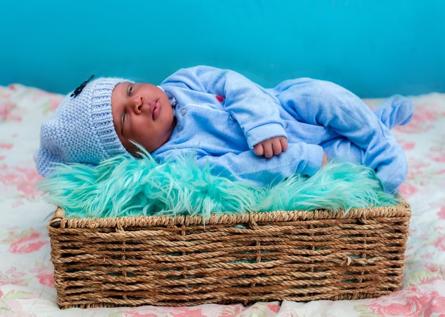 Baby resting in a woven basket wearing a onesie