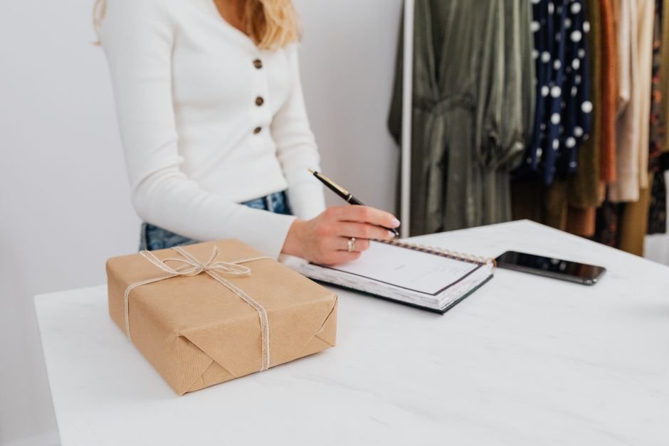 Woman writing a note beside a wrapped client gift box on a desk