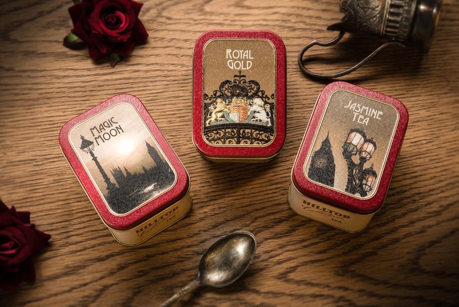 Three tins of loose leaf tea arranged on a wooden surface with a vintage spoon