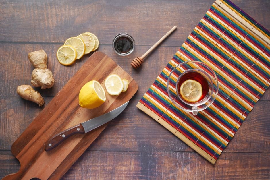 A flat lay of ginger tea with lemon slices and a honey dipper on a wooden board