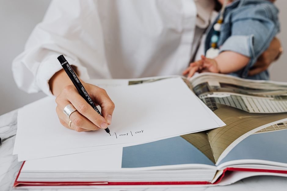 New mother writing a keepsake note while holding her baby