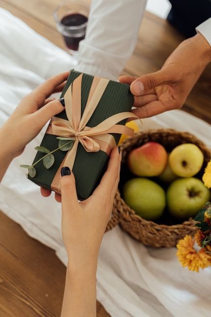 Hands exchanging a corporate holiday gift basket beside fresh fruit on a table