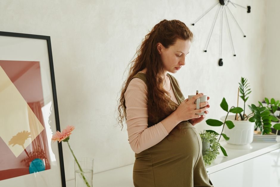 Pregnant woman relaxing with a warm cup of tea, a comfort item worth including in a pregnancy care package
