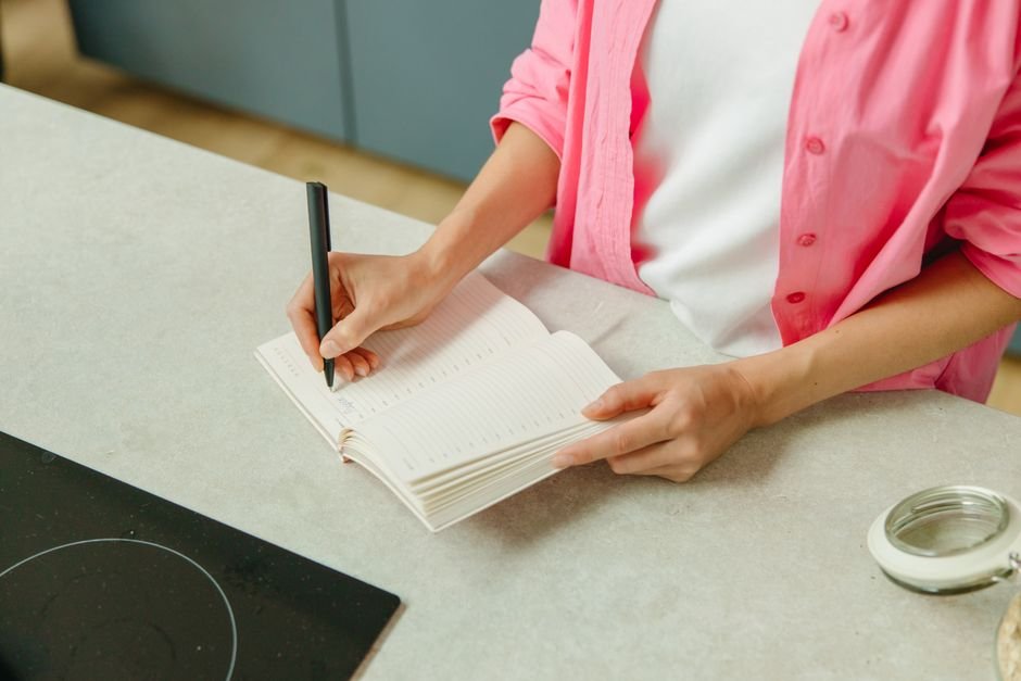 Woman writing her birthday wish list in a notebook at the kitchen counter